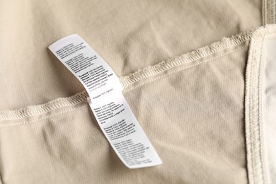 Photo of Clothing label on beige garment as background, above view