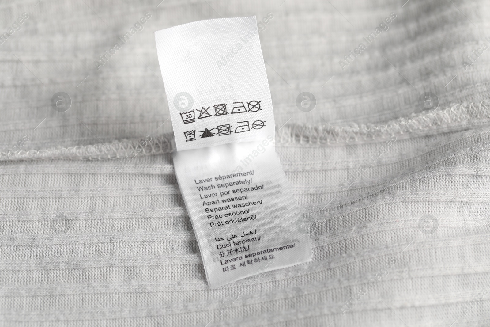 Photo of Clothing label with care symbols on light garment as background, closeup