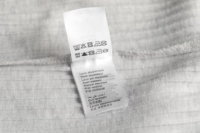 Photo of Clothing label with care symbols on light garment as background, closeup