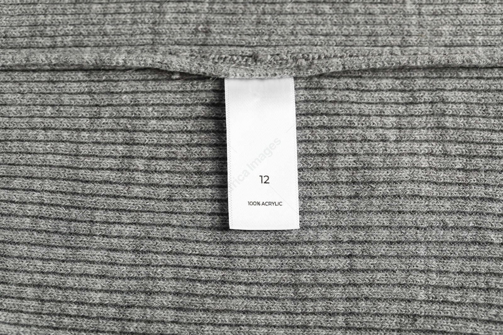 Photo of Clothing label with size and material content on grey garment as background, top view