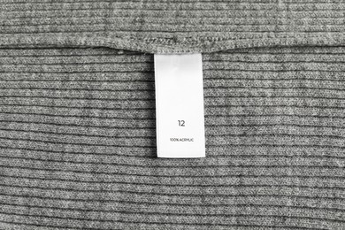 Photo of Clothing label with size and material content on grey garment as background, top view