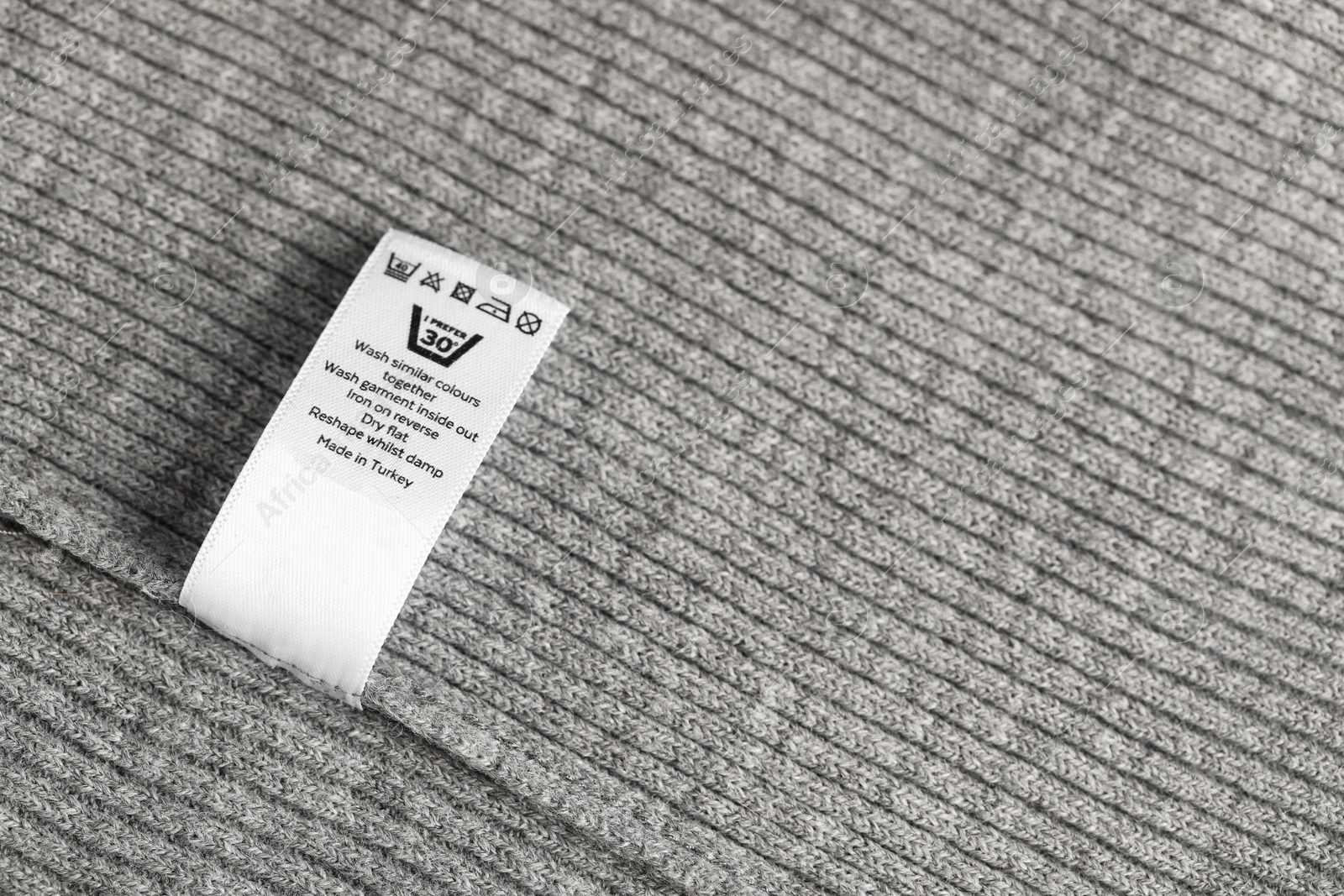 Clothing label with care symbols on grey garment as background, top view Photo of Clothing label with care symbols on grey garment as background, top view