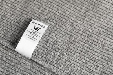 Photo of Clothing label with care symbols on grey garment as background, top view