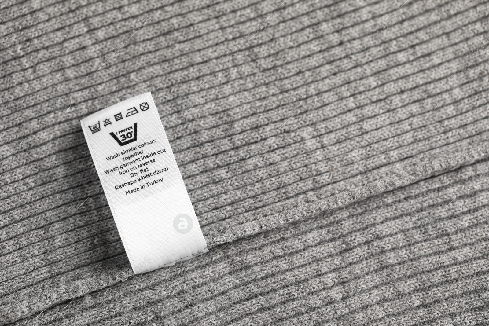 Clothing label with care symbols on grey garment as background, top view Photo of Clothing label with care symbols on grey garment as background, top view