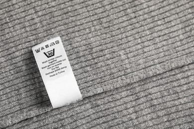 Photo of Clothing label with care symbols on grey garment as background, top view