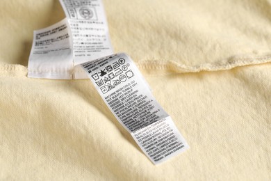 Photo of Clothing label with care symbols on yellow garment as background, closeup