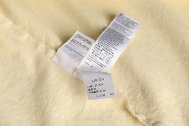 Photo of Clothing label with size on yellow garment as background, above view