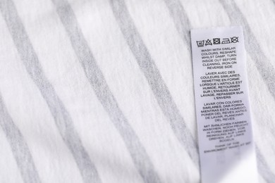 Photo of Clothing label with care symbols on striped garment as background, closeup