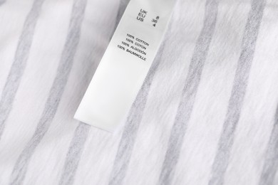 Photo of Clothing label with size and material content on striped garment as background, closeup