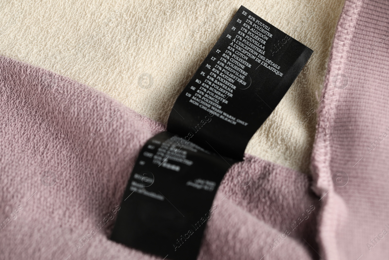 Photo of Clothing label with material content on color garment as background, closeup