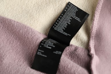 Photo of Clothing label with material content on color garment as background, closeup