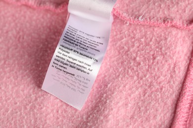 Photo of Clothing label with material content on pink garment as background, above view
