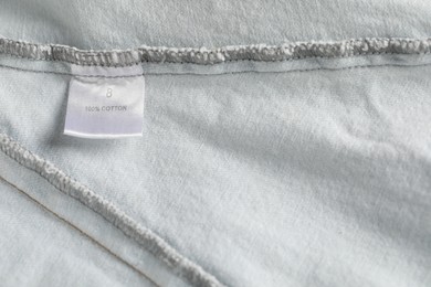 Photo of Clothing label with size and material content on garment as background, top view