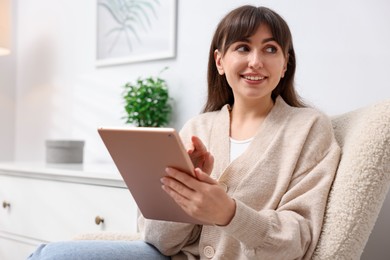 Photo of Woman using modern tablet in armchair at home. Space for text