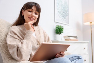 Photo of Woman using modern tablet in armchair at home. Space for text