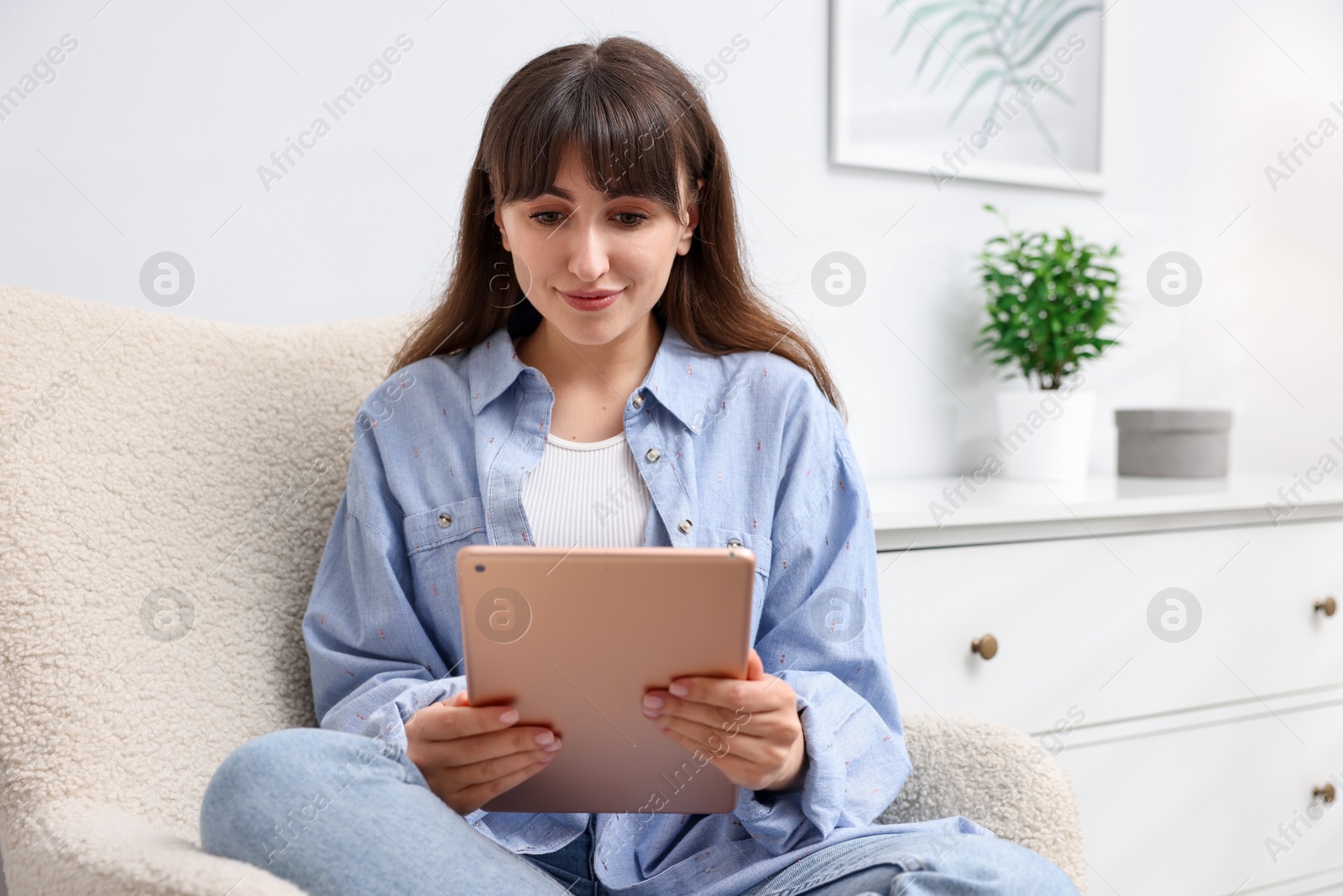 Photo of Woman using modern tablet in armchair at home