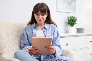 Photo of Woman using modern tablet in armchair at home