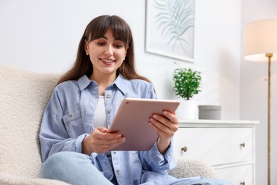 Photo of Woman using modern tablet in armchair at home