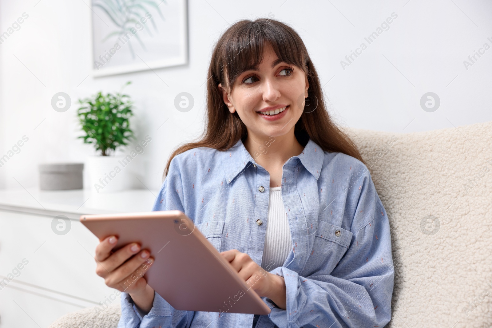 Woman using modern tablet in armchair at home Photo of Woman using modern tablet in armchair at home