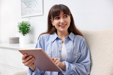 Photo of Woman using modern tablet in armchair at home