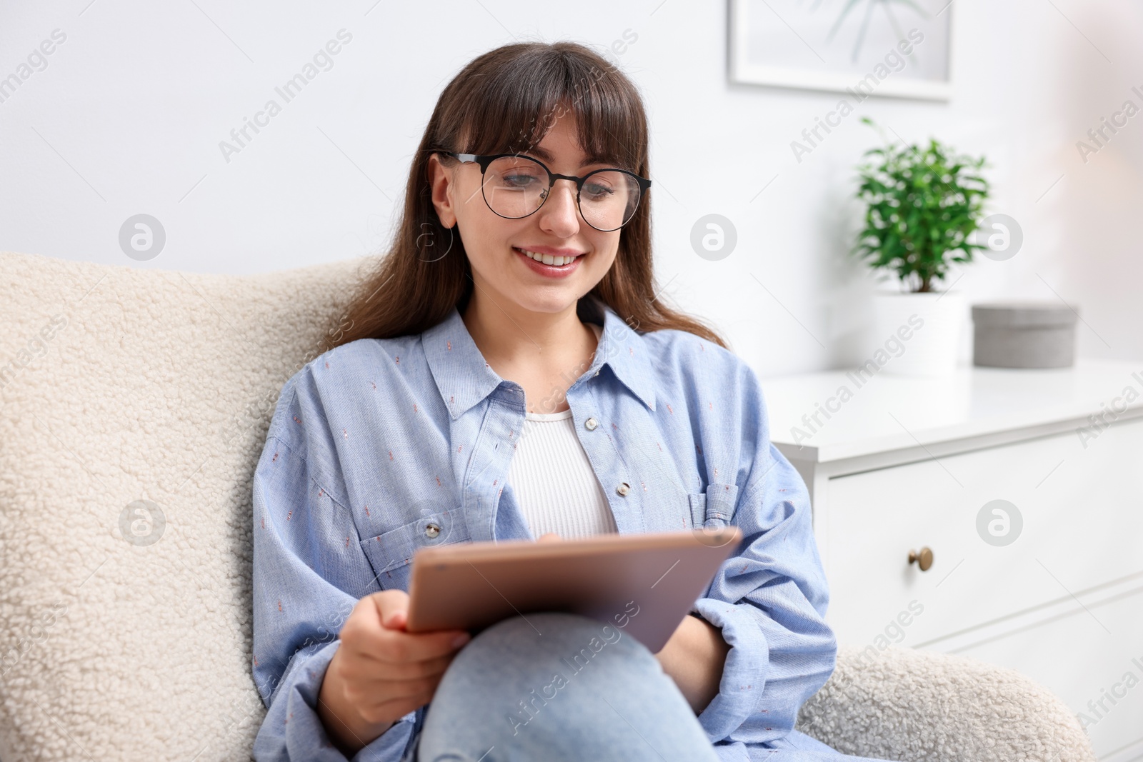 Woman using modern tablet in armchair at home Photo of Woman using modern tablet in armchair at home