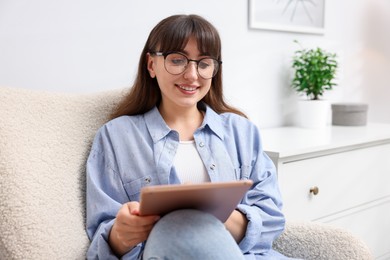 Photo of Woman using modern tablet in armchair at home