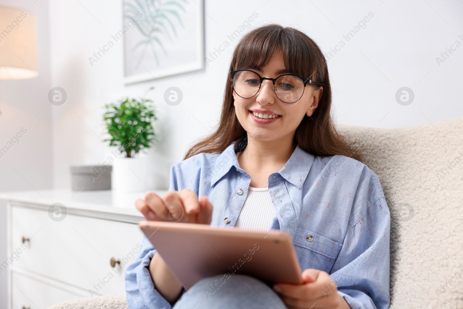 Woman using modern tablet in armchair at home Photo of Woman using modern tablet in armchair at home