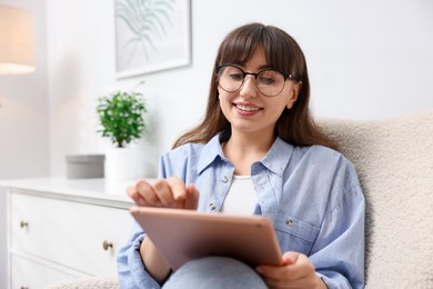 Photo of Woman using modern tablet in armchair at home