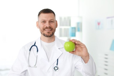 Photo of Nutritionist with green apple and stethoscope in clinic, selective focus