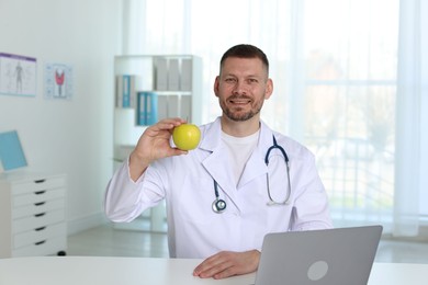 Photo of Nutritionist with green apple and stethoscope at table in clinic