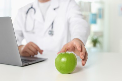Photo of Nutritionist taking green apple at table in clinic, closeup