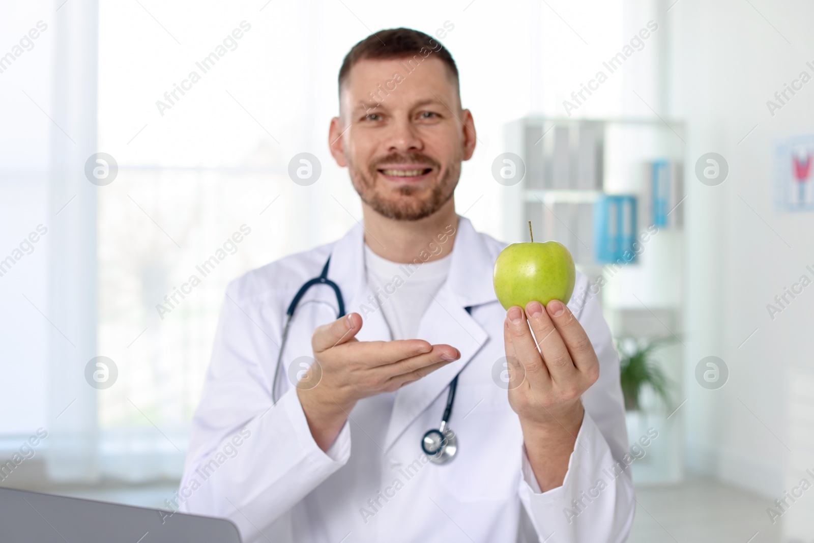 Photo of Nutritionist with green apple and stethoscope in clinic, selective focus