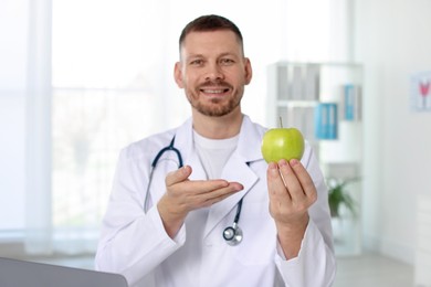 Photo of Nutritionist with green apple and stethoscope in clinic, selective focus