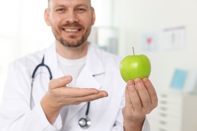 Photo of Nutritionist with green apple and stethoscope in clinic, selective focus