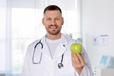 Photo of Nutritionist with green apple and stethoscope in clinic, selective focus