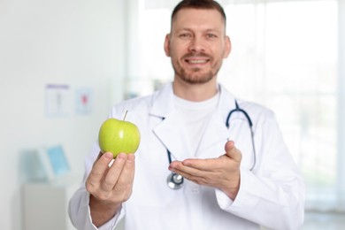 Photo of Nutritionist with green apple and stethoscope in clinic, selective focus