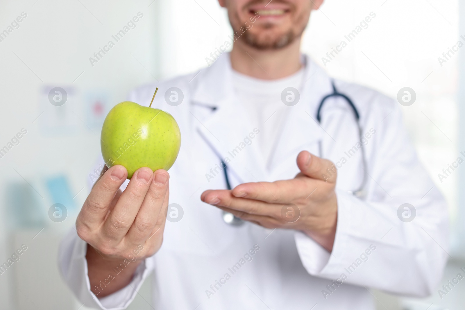 Photo of Nutritionist with green apple and stethoscope in clinic, selective focus