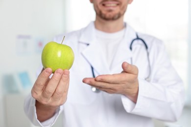 Photo of Nutritionist with green apple and stethoscope in clinic, selective focus