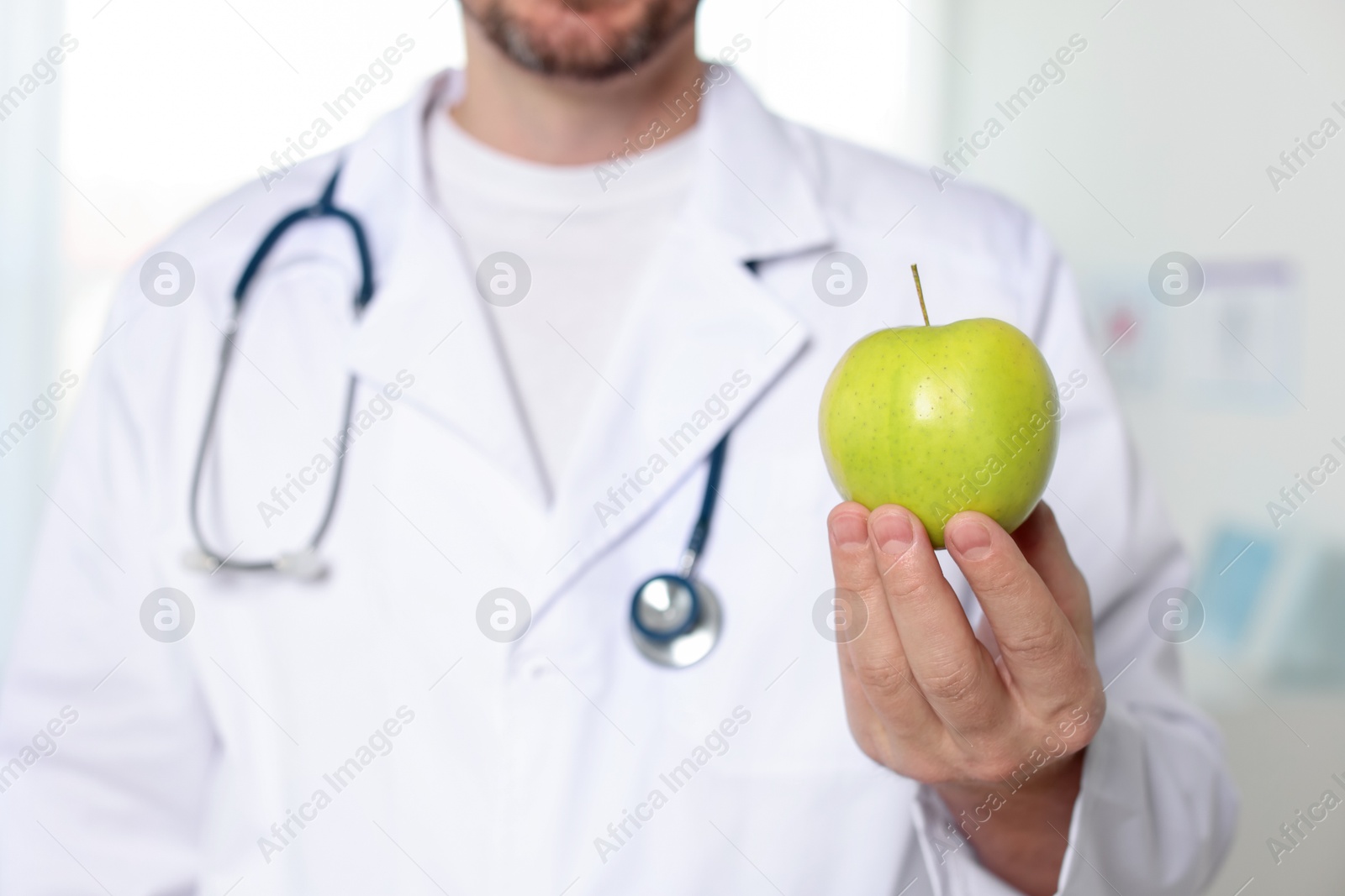 Photo of Nutritionist with green apple and stethoscope in clinic, selective focus