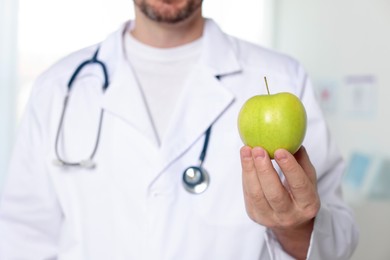 Photo of Nutritionist with green apple and stethoscope in clinic, selective focus