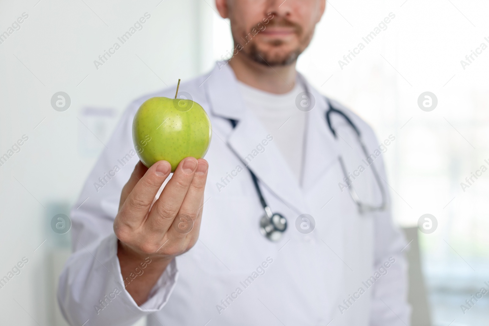 Photo of Nutritionist with green apple and stethoscope in clinic, selective focus
