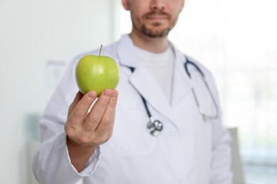 Photo of Nutritionist with green apple and stethoscope in clinic, selective focus