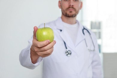 Photo of Nutritionist with green apple and stethoscope in clinic, selective focus