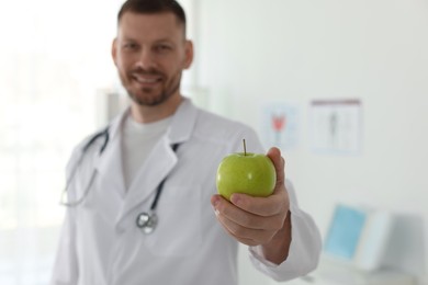 Photo of Nutritionist with green apple and stethoscope in clinic, selective focus