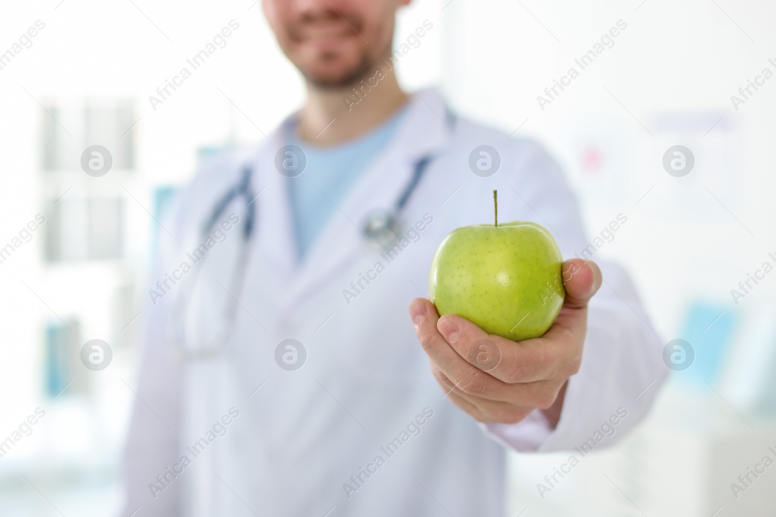 Photo of Nutritionist with green apple and stethoscope in clinic, selective focus