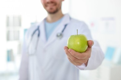 Photo of Nutritionist with green apple and stethoscope in clinic, selective focus