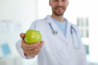 Photo of Nutritionist with green apple and stethoscope in clinic, selective focus