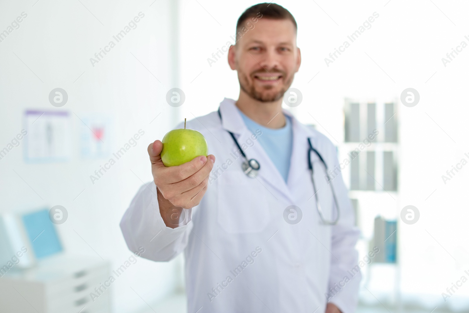 Photo of Nutritionist with green apple and stethoscope in clinic, selective focus