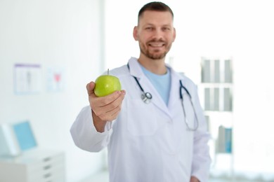 Photo of Nutritionist with green apple and stethoscope in clinic, selective focus