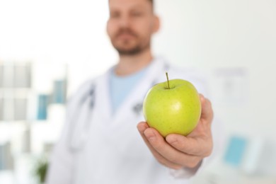Photo of Nutritionist with green apple and stethoscope in clinic, selective focus